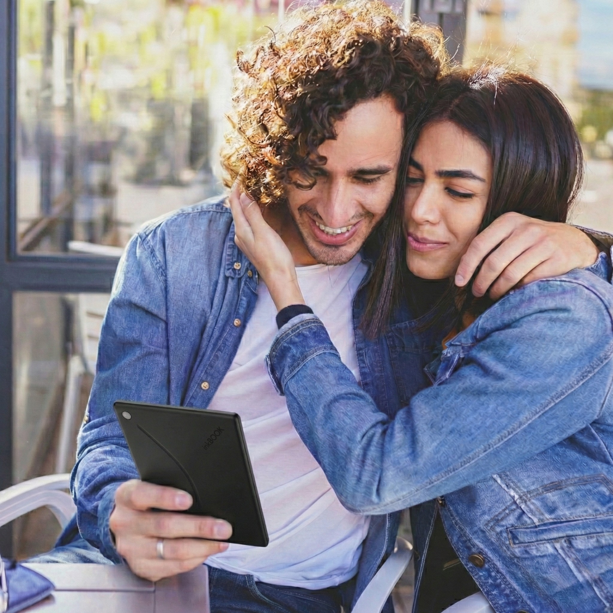 Couple sitting together, looking at a inkBOOK reader device outdoors.